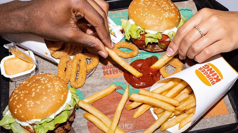Burger King Whopper sits next to a Whopper Jr. as people eat fries