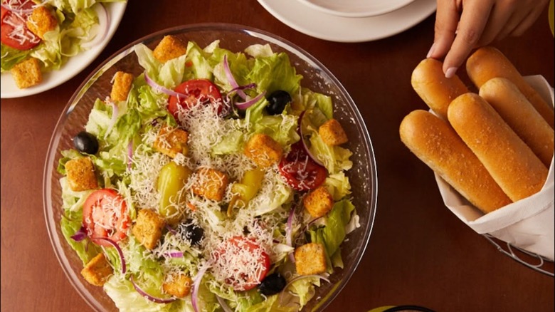 Someone reaches for a breadstick next to a bowl of salad.