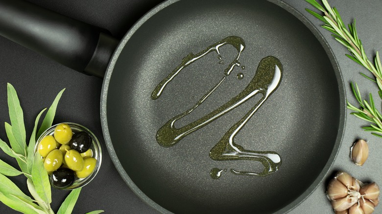 Olive oil in a pan surrounded by olives garlic rosemary