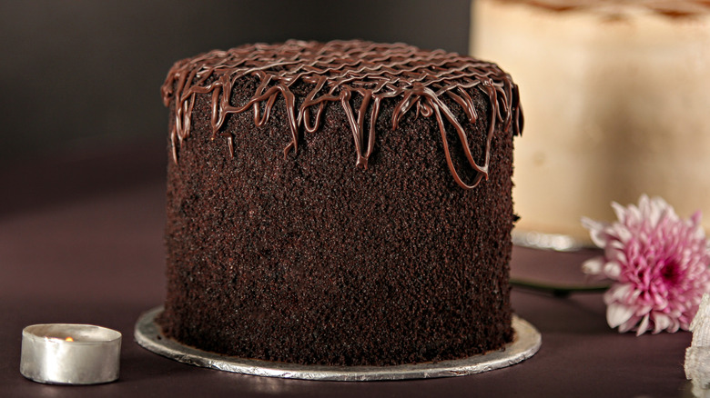 A tall chocolate cake with another white-iced cake in the background