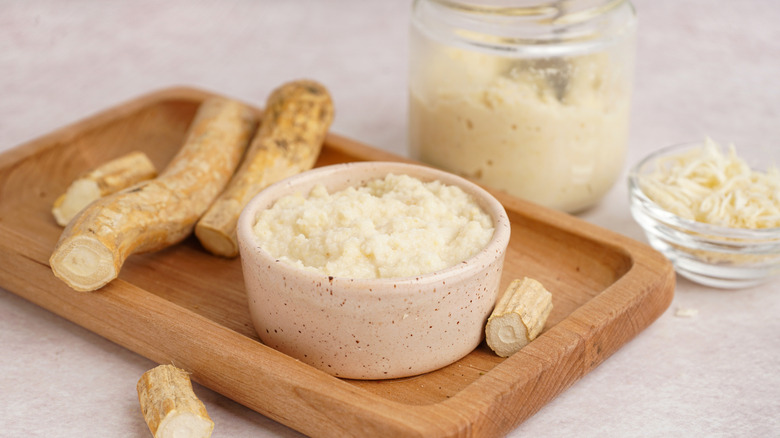 Fresh grated horseradish in multiple bowls, surrounded by uncut horseradish root