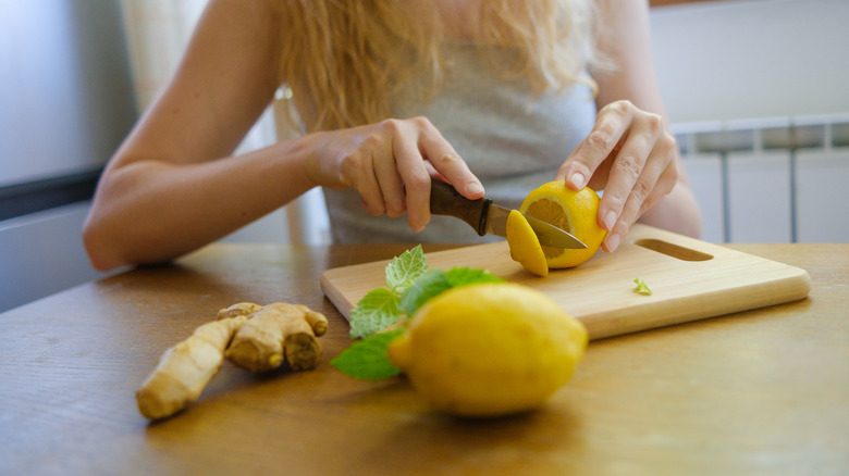 A woman cuts lemons on a wooden cutting board, while a knob of ginger sits closeby
