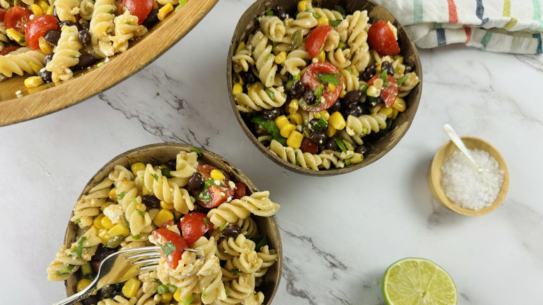 two bowls of pasta salad next to a serving of salt and fresh lime.