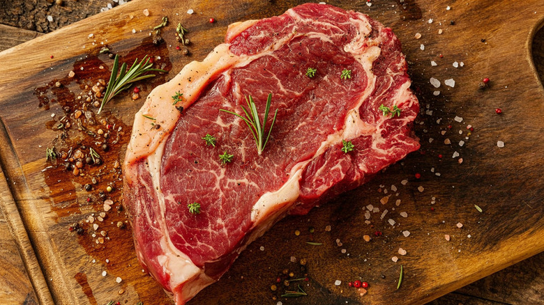 A ribeye with fresh rosemary and thyme on a wooden cutting board.
