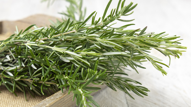 Sprigs of rosemary on a wooden cutting board.