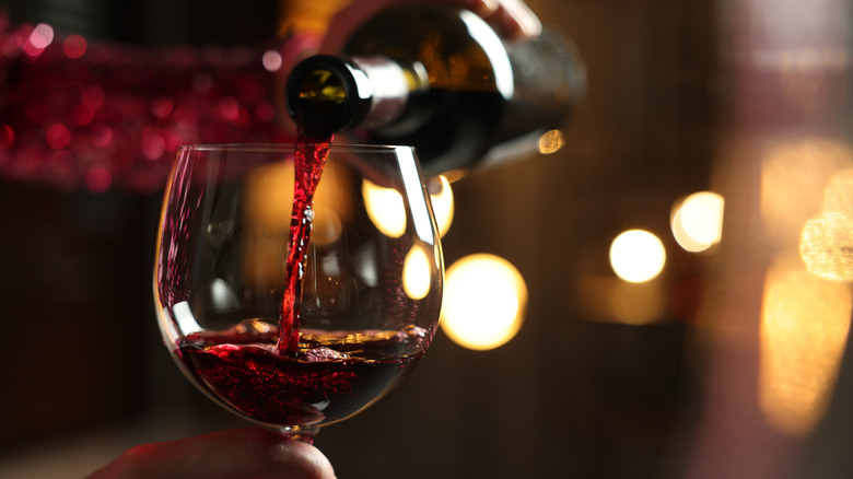 A bottle of red wine being poured into a glass.