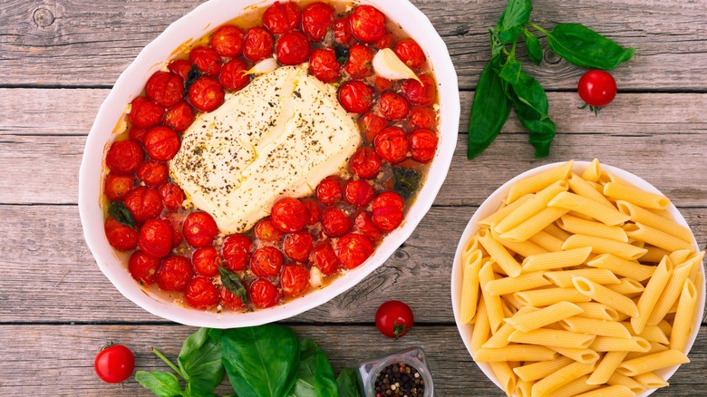 Tomato and cheese dish next to bowl of pasta