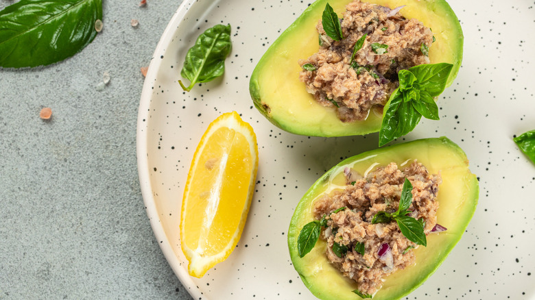 Avocado stuffed with tuna salad with a wedge of lemon on a white speckled plate