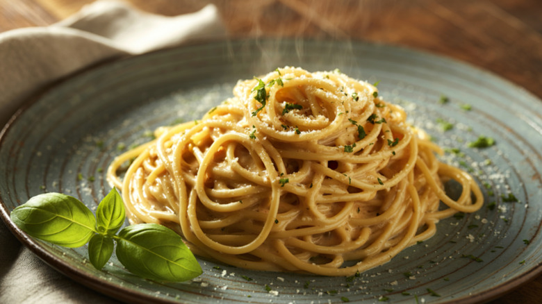 A plate of spaghetti with creamy alfredo sauce is topped with fresh cheese and herbs, with a few sprigs of basil on the side
