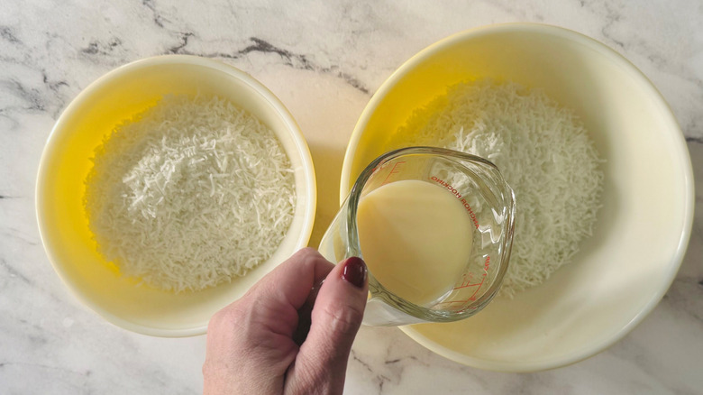 Hand pouring milk into bowl of shredded coconut