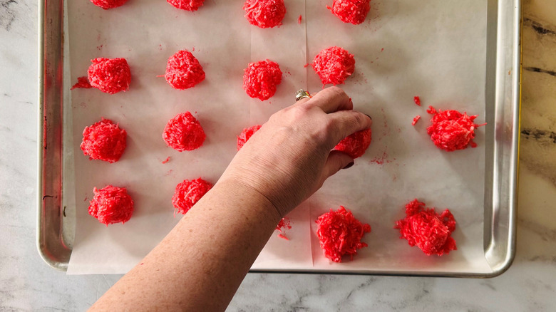 Hand grabbing red Jell-O ball on baking sheet