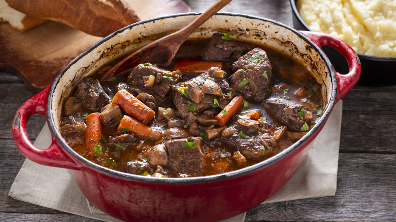 A pot of beef stew on a table with a wooden spoon