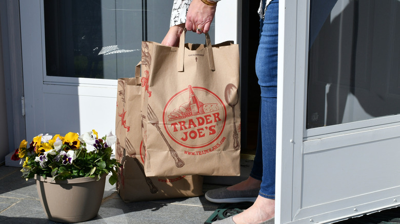 Person carrying paper Trader Joe's bags into their house