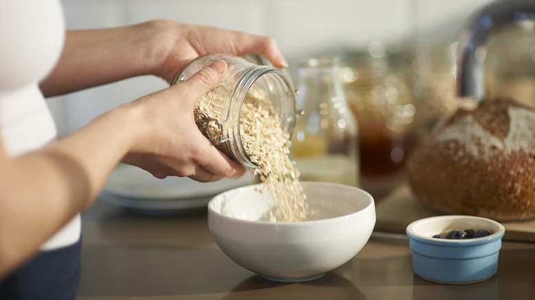 A person pours oats into a white bowl in the kitchen