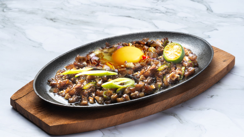 A sizzling platter of sisig served on wooden cutting board.