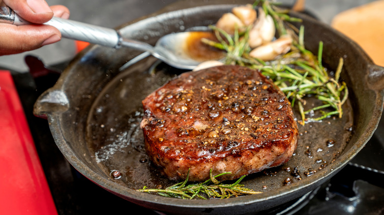 Steak cooking in pan with garlic and thyme.