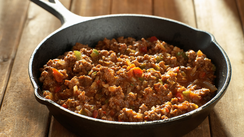 Sloppy Joe mix cooked in an iron skillet on top of a wooden table.