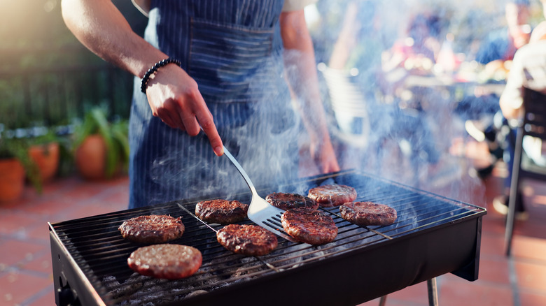 Person grilling burgers over charcoal.