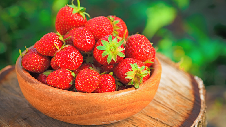A wooden bowl containing ripe strawberries.