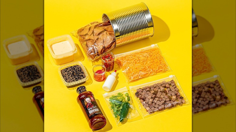 All the fixings for Guy Fieri's trashcan nachos, including the can, tortilla chips, beans, cheese, and sauce