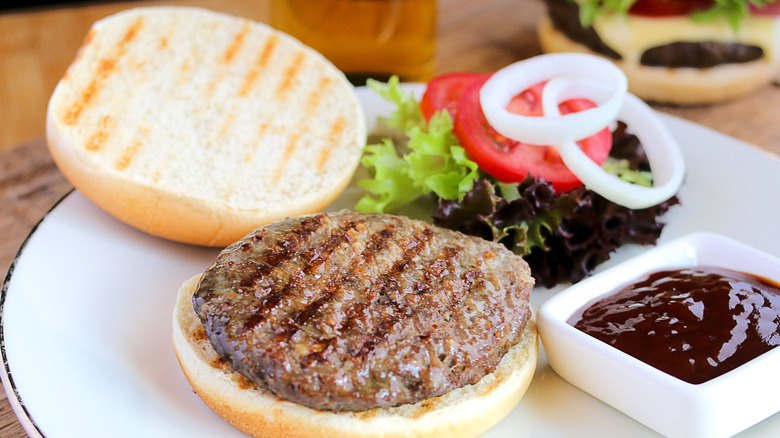 A toasted burger bun next to a burger and toppings