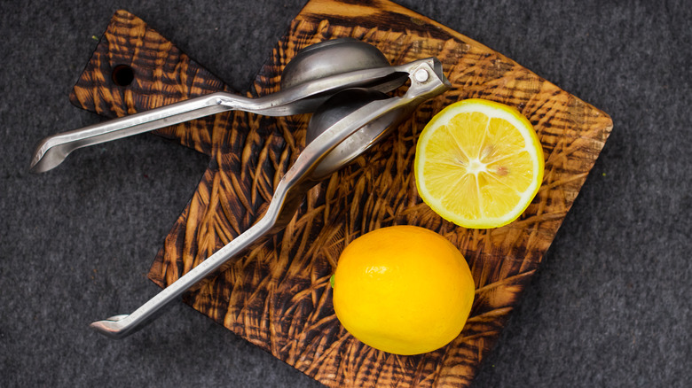 Handheld metal lemon juicer with lemons on cutting board