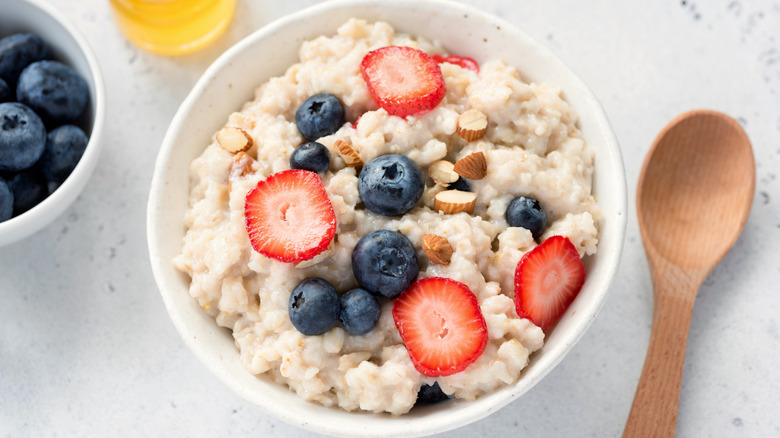 A bowl of oatmeal is topped with strawberries, nuts, and blueberries.