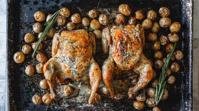 Two Cornish hens with baby potatoes on a baking sheet.