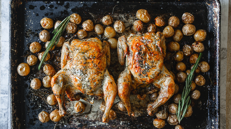 Two Cornish hens with baby potatoes on a baking sheet.