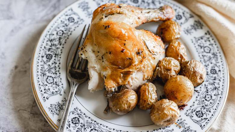A Cornish hen quarter on a plate with baby potatoes and fork.