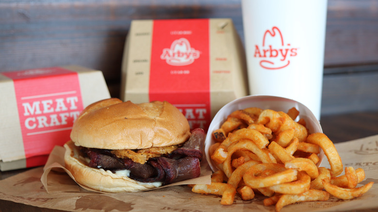 An Arby's fast food meal of a sandwich and curly fries sits on a wooden table