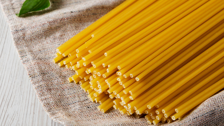 A bundle of dry bucatini sits on a large cloth.