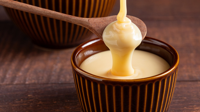 A spoon scoops out some sweetened condensed milk from a small bowl