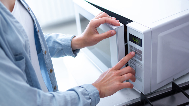Woman using microwave to cook food in kitchen