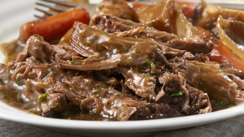 Shredded pot roast sits on a plate, smothered in gravy