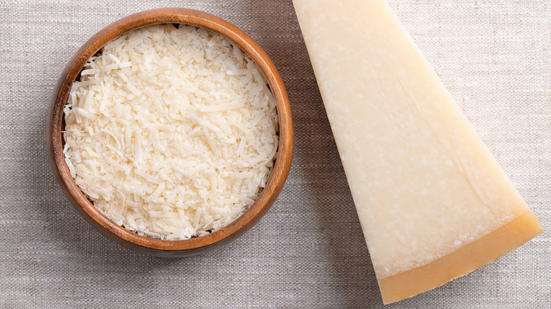 Grated parmesan cheese sits next to a wedge.