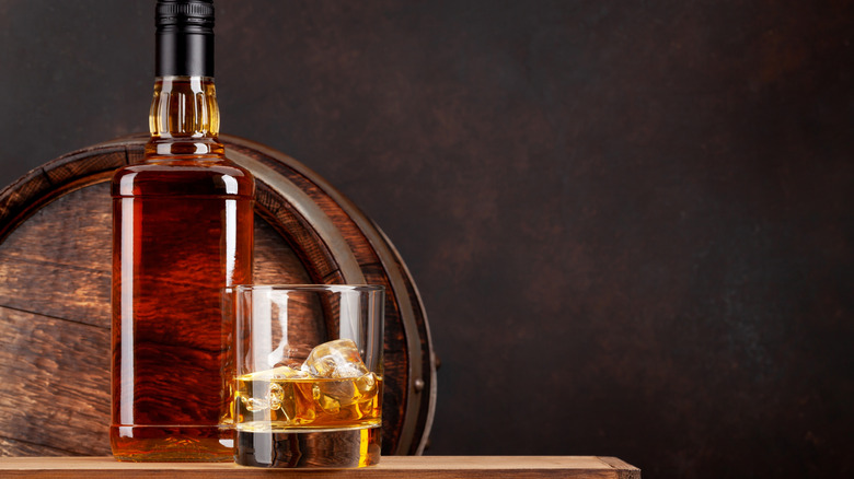 A glass of Scotch rests next to a bottle.