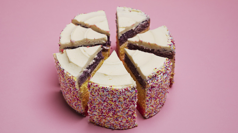 A birthday cake cut into seven pieces against a pink background