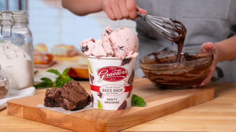 Scoops of Graeter's Minty Brownie ice cream overflow the pint as a person mixes brownie batter
