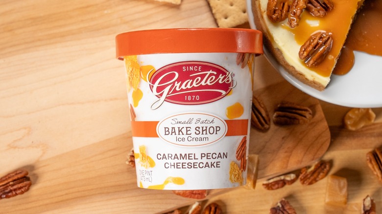 A Graeter's pint of Caramel Pecan Cheesecake ice cream on a wooden surface with cheesecake