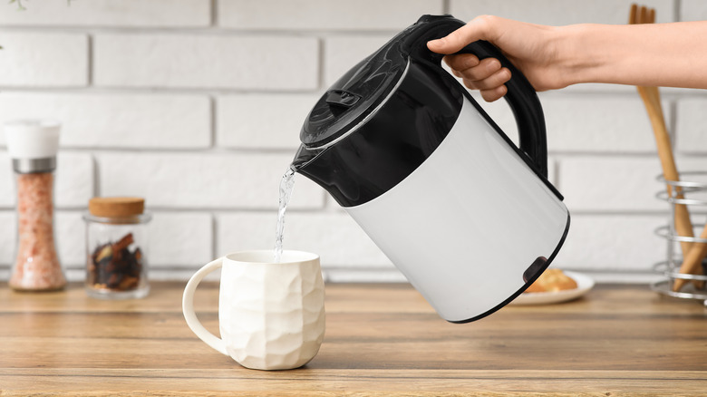 Someone pours water from an electric kettle into a cup.