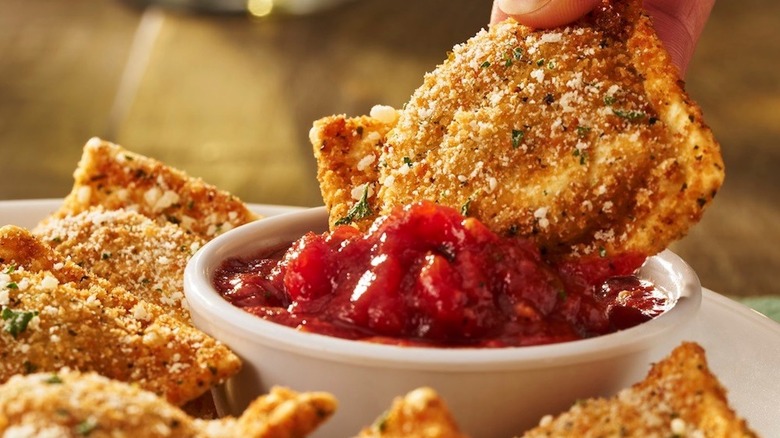 An Olive Garden toasted ravioli gets dipped in marinara sauce