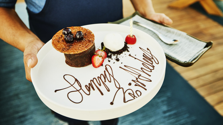 A restaurant server holds a dessert plate with 'Happy Birthday' written in chocolate syrup