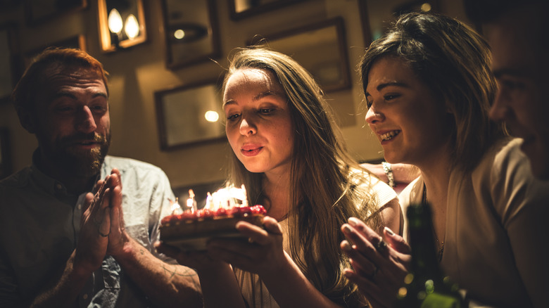 The friends celebrate a birthday over a cake with candles in a restaurant