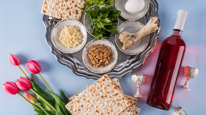 Traditional Jewish Passover foods on seder plate with matzo, wine, and flowers