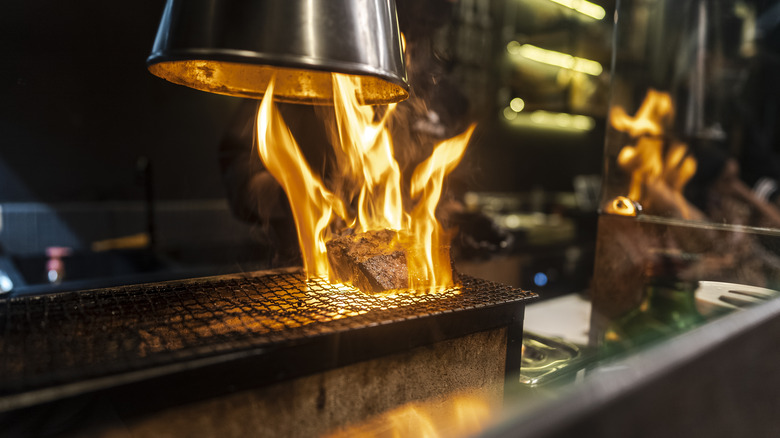 Meat roasting on an open flame grill under a lamp