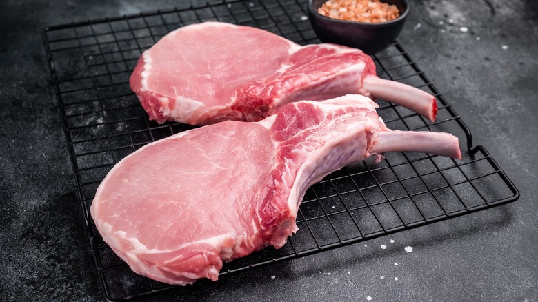 Raw bone-in pork chops sit on a wire rack