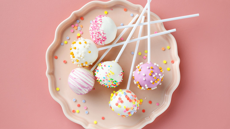 Several cake pops sit, covered in sprinkles and icing drizzle