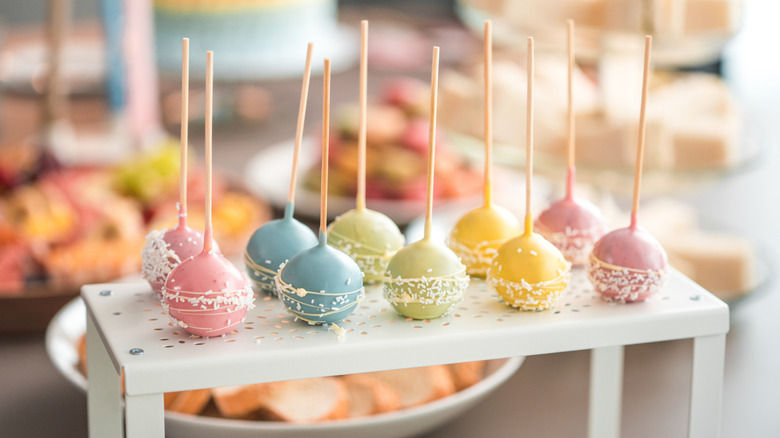 A few pastel colored cake pops with sprinkles sit on a small white table