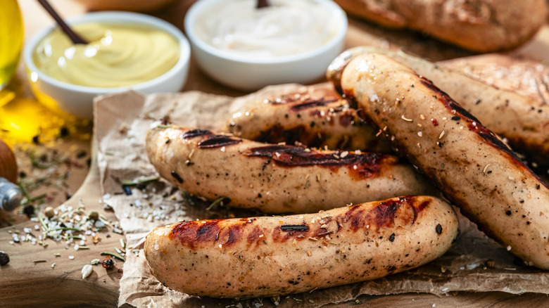 Grilled bratwurst on a cutting board with condiments.